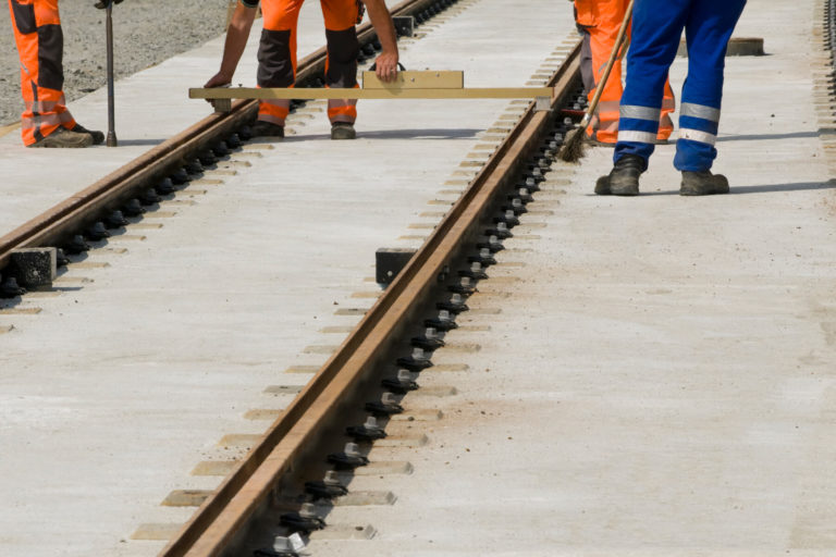 Mehrer Arbeiter halten eine Messlatte zwischen die Gleise.