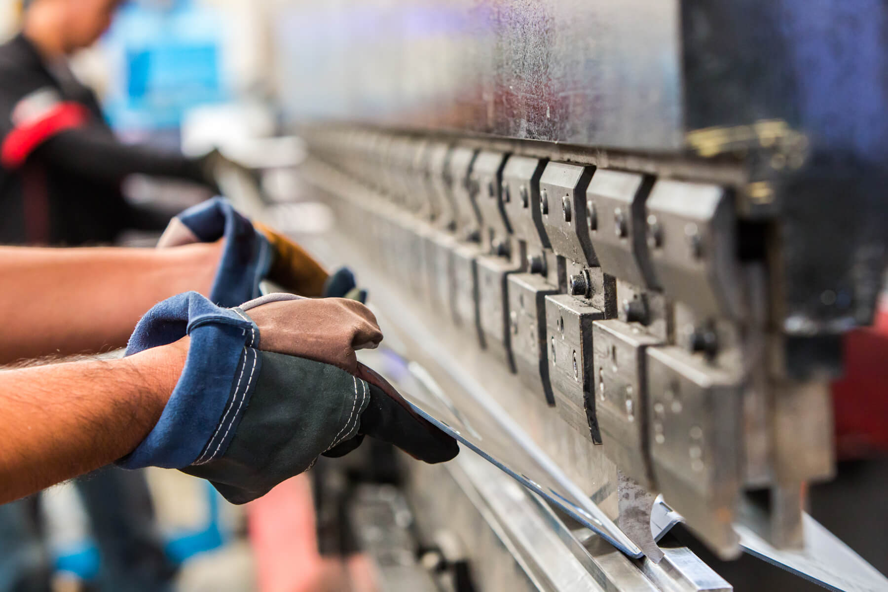 Arbeiter mit Handschuhen halten eine Metallplatte in eine Maschine zum Stanzen oder Schneiden.