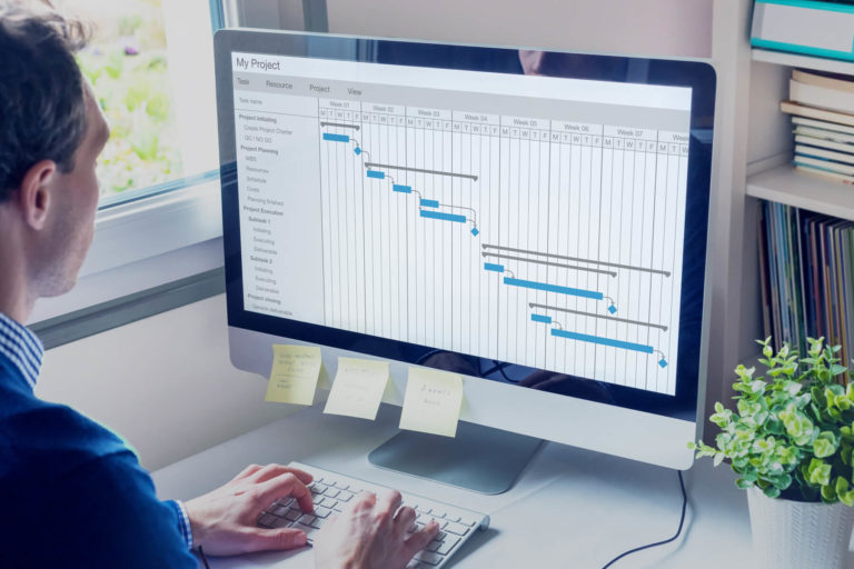 Ein Mann schaut auf den Bildschirm auf dem ein Kalender abgebildet ist. Außerdem tippt er auf der Tastatur.